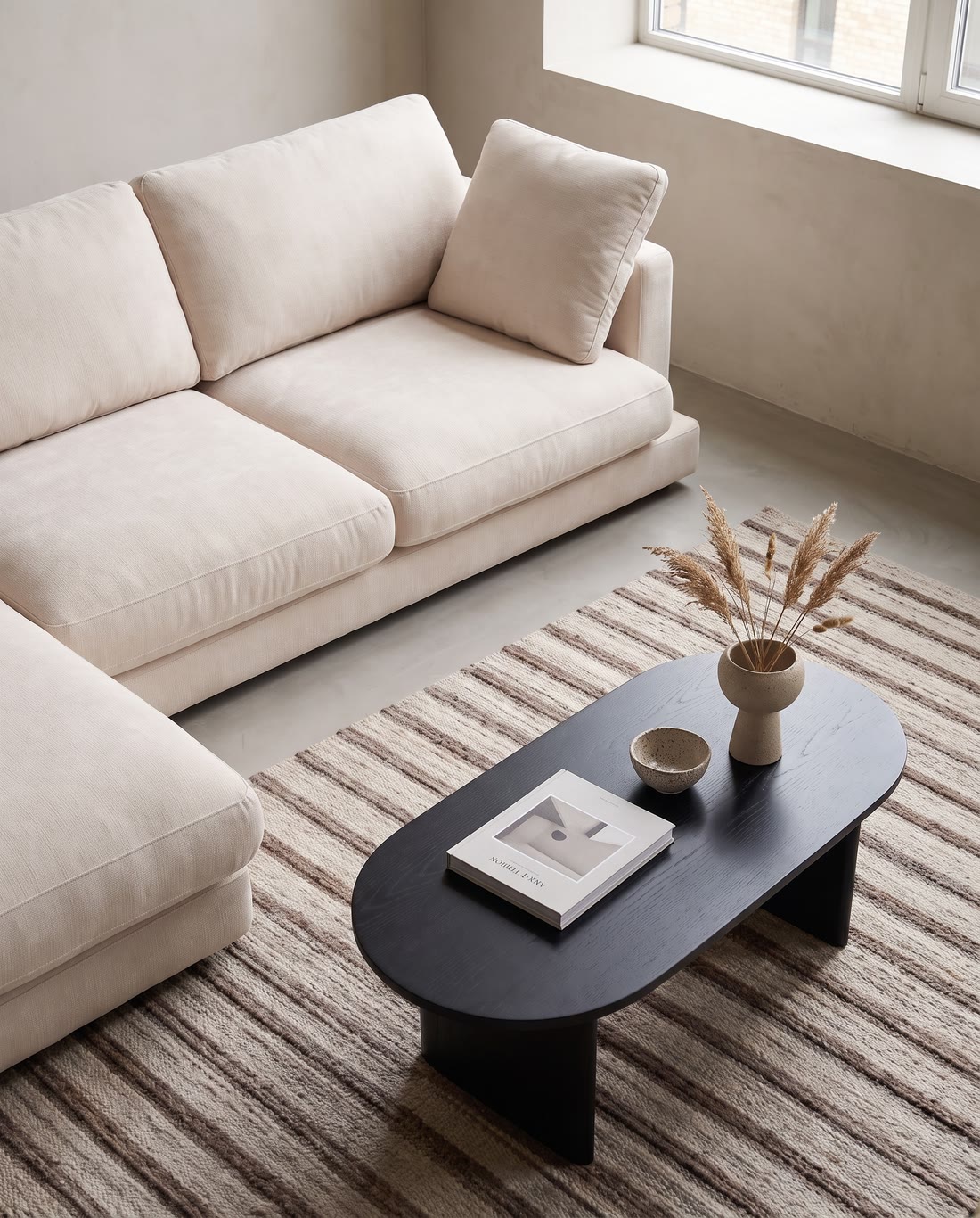 A curved cream sofa beside a wooden sideboard in a daylit room.