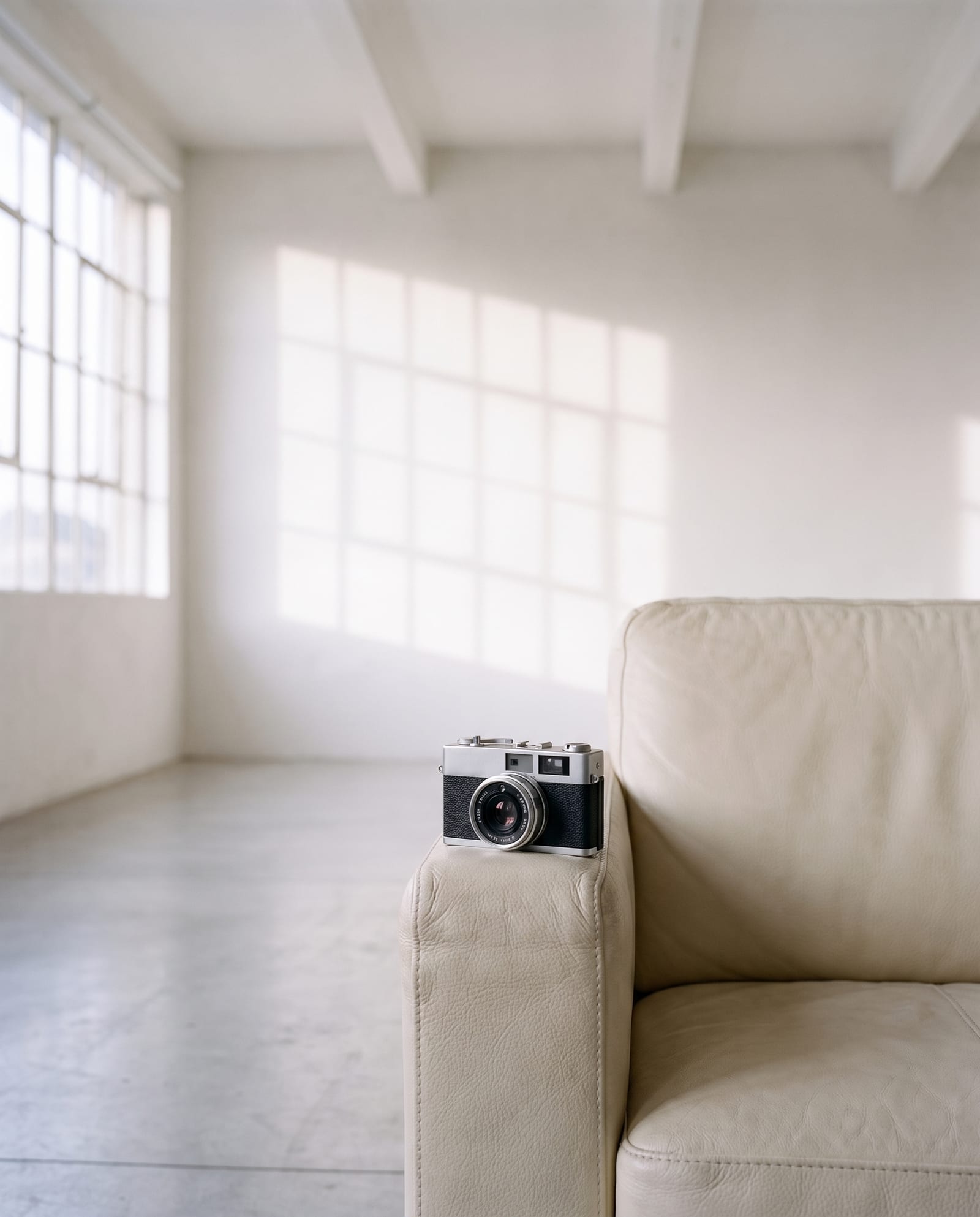 A rangefinder camera resting on the arm of a pale leather sofa in a daylit loft.